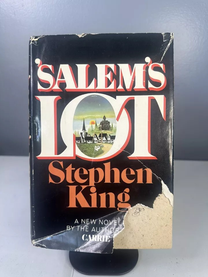 The image shows a worn cover of Stephen King's novel "'Salem's Lot." The title is in large white and red text against a black background. The cover features a small illustration of a town, partially torn at the bottom corner.