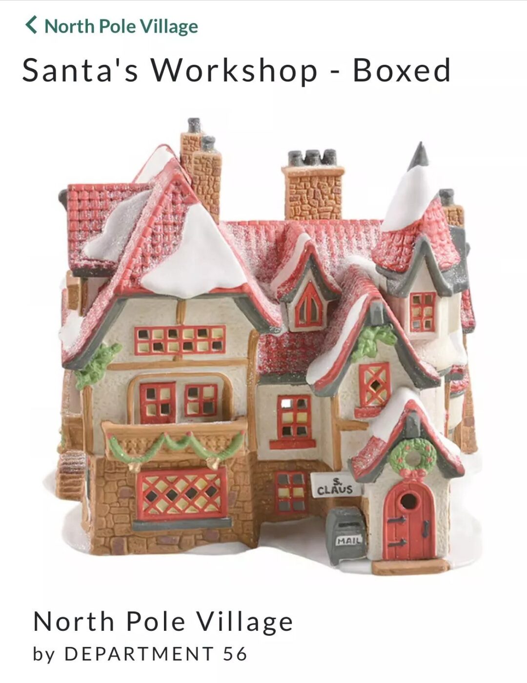 A ceramic model of Santa's Workshop from North Pole Village, featuring a snow-covered roof, red and tan brick design, and detailed windows. The sign on the door reads "Claus.