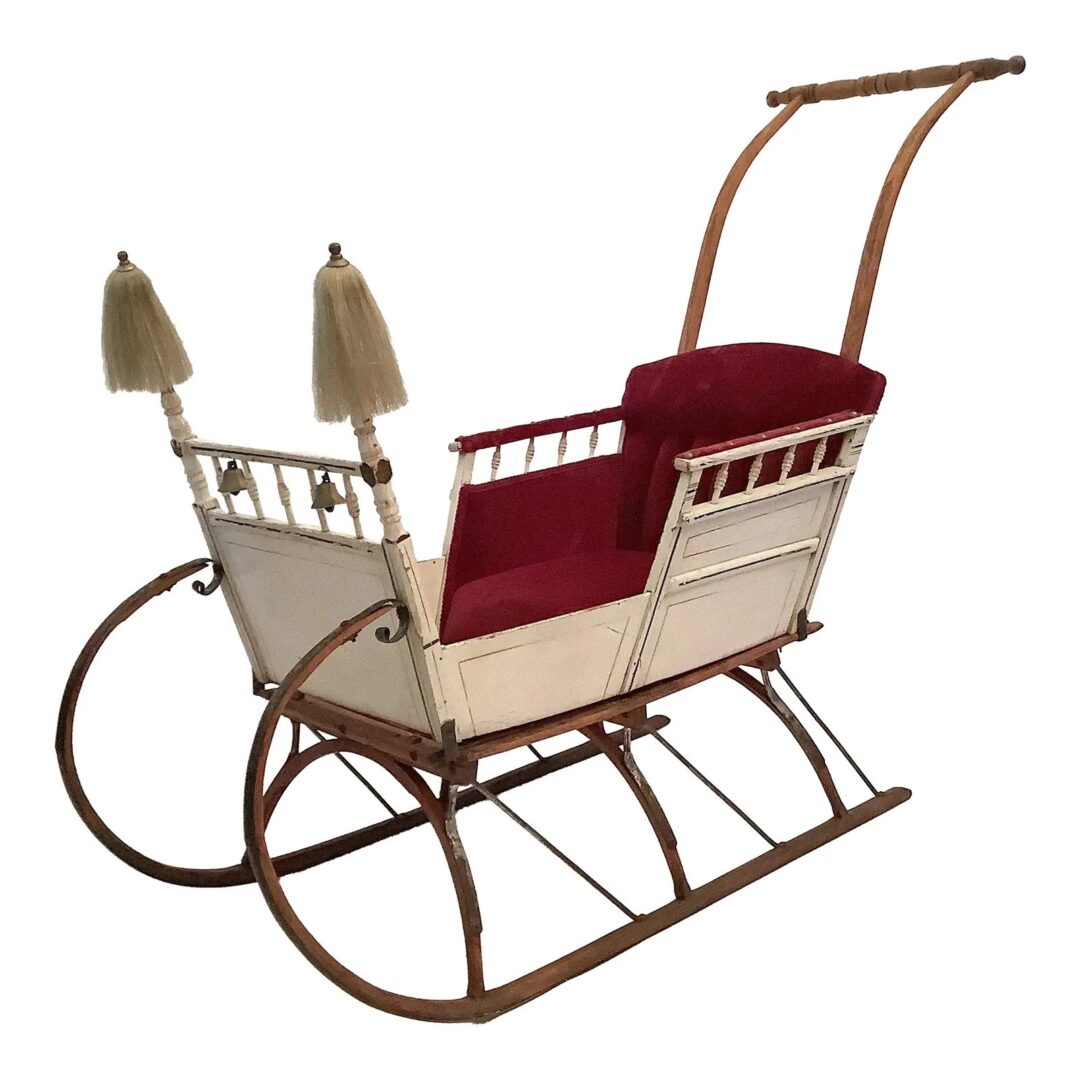 A vintage white sleigh with wooden runners and a red cushioned seat. It features decorative finials and an arched handle at the back.