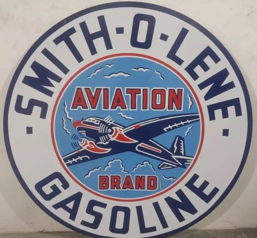 A vintage-style sign featuring the text "Smith-O-Lene Aviation Brand Gasoline." The design includes an illustration of an airplane flying above clouds in a circular frame. The colors are predominantly blue, red, and white.