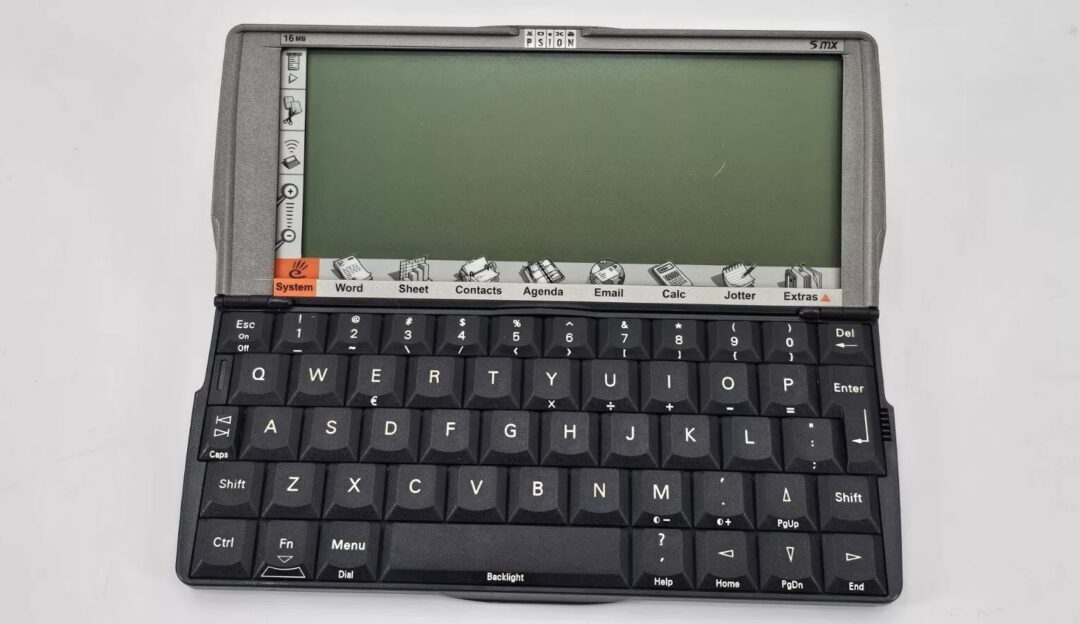 A vintage Psion 5mx handheld personal digital assistant with a black QWERTY keyboard and a monochrome display. The screen shows menu icons for Word, Sheet, Contacts, Agenda, Email, Calc, Jotter, and Extras.