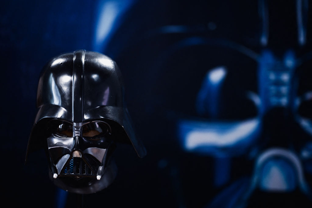 A black helmet with a glossy finish, resembling a famous sci-fi character, is centered against a dark, blurred background, creating a dramatic and mysterious atmosphere.