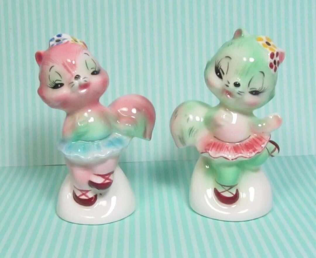 Two ceramic animal figurines with pastel colors, one pink and the other green, wearing tutus and bows. They stand on a striped light blue background, giving a whimsical and vintage look.