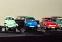 Three vintage model cars are displayed on black platforms. The cars are mint green, blue, and red, lined up in a row. The background is blurred, drawing attention to the detailed miniature vehicles in the foreground.