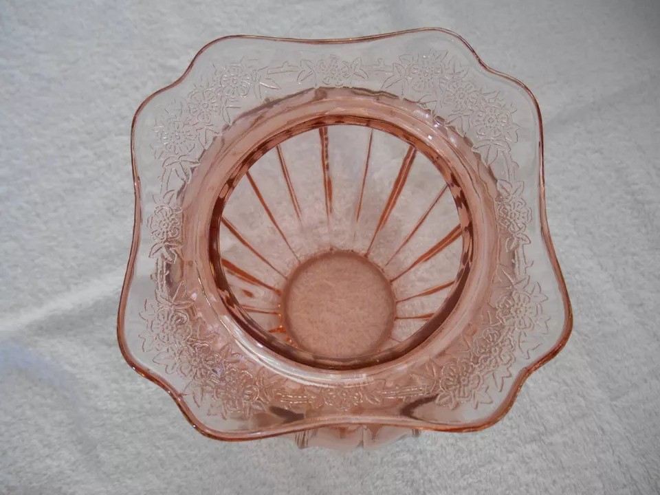 A top view of an empty pink glass bowl with ornate floral patterns along the rim, placed on a white surface. The bowl has a scalloped edge and vertical lines from the center to the edge.