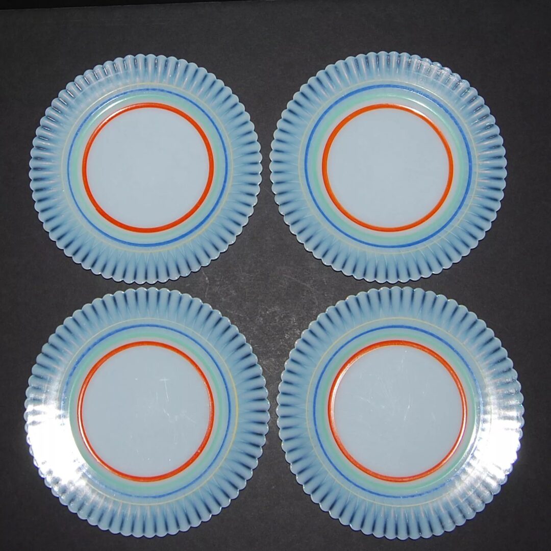 Four decorative plates with blue ridges and orange rings are arranged symmetrically in a two-by-two grid on a dark background.