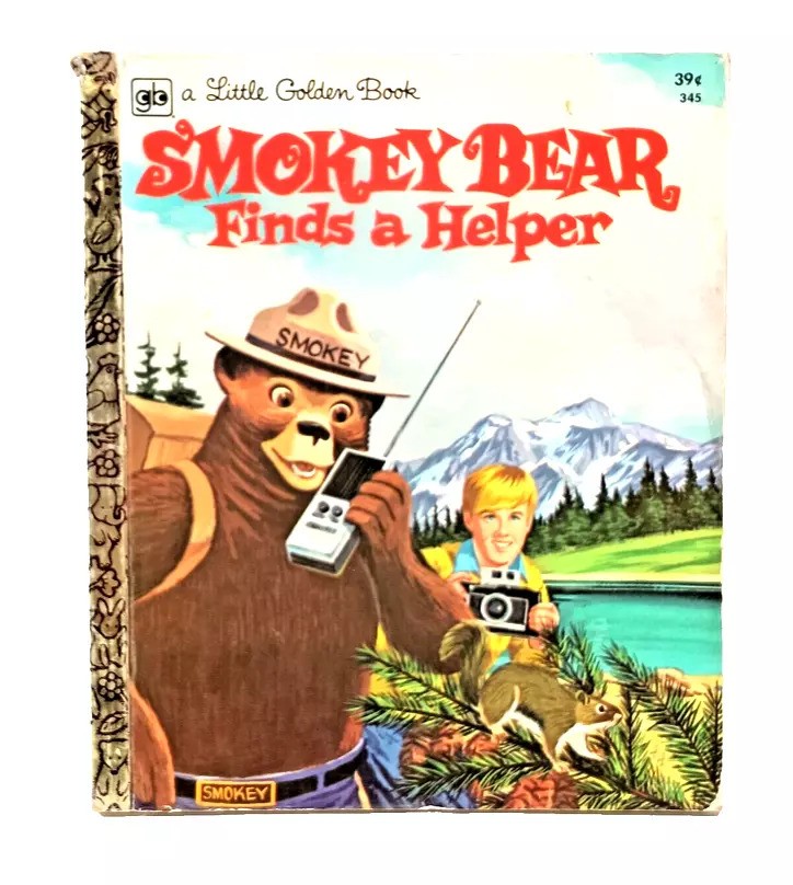 Cover of "Smokey Bear Finds a Helper," a Little Golden Book. Smokey Bear is using a radio, with a boy holding a camera beside him. They stand by a forest stream with mountains in the background.