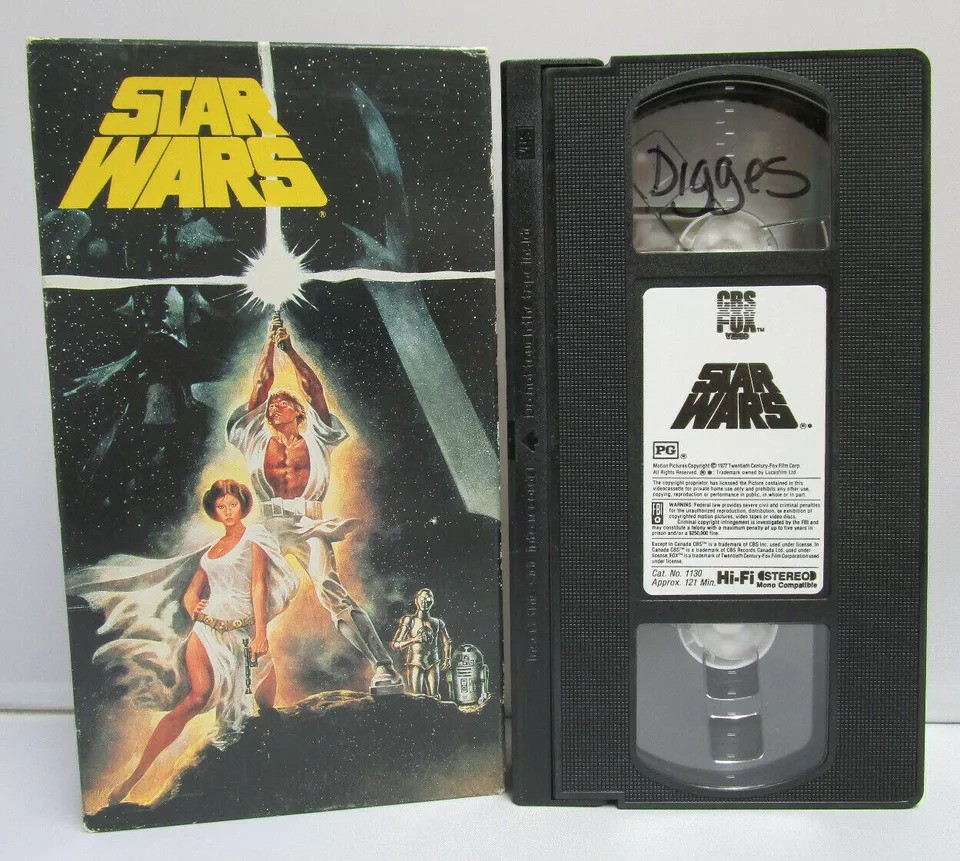 A vintage "Star Wars" VHS tape with its cover. The cover features characters holding lightsabers with a dramatic space background. The VHS tape is labeled with handwriting.