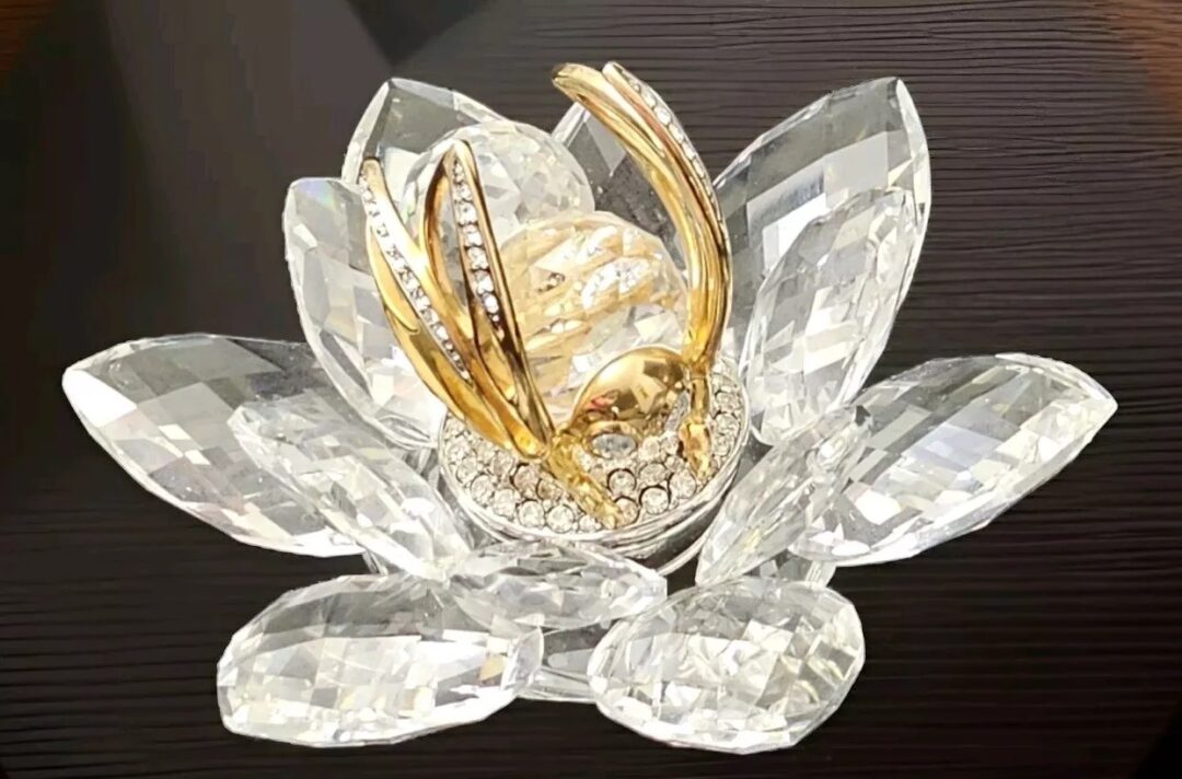 A decorative crystal lotus flower with gold and diamond accents on a dark background. The petals are intricately cut, and the centerpiece features gold-plated details encrusted with sparkling gems.