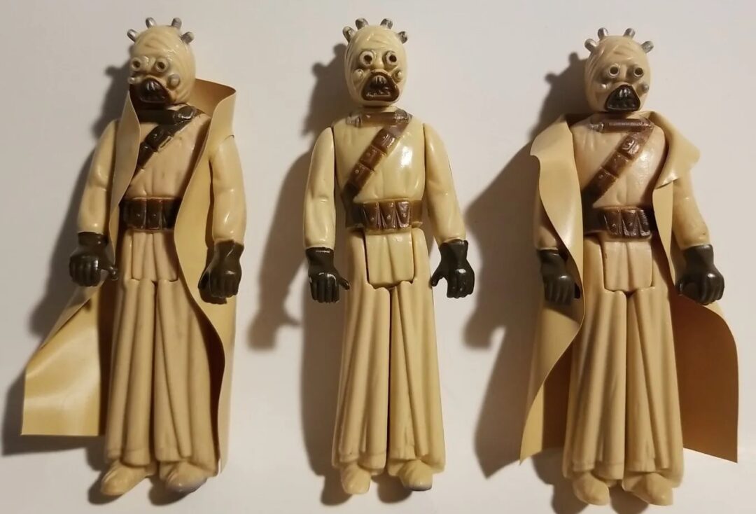 Three vintage action figures of Tusken Raiders, also known as Sand People, from the Star Wars universe. They are wearing tan robes with brown accessories and have detailed, mask-like faces.