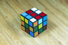 A partially solved Rubik's Cube with mixed colors on a wooden surface. The top face has red, blue, and white tiles.