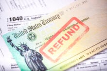 A United States Treasury check labeled "REFUND" is placed atop a 1040 tax form. The check features an image of the Statue of Liberty.