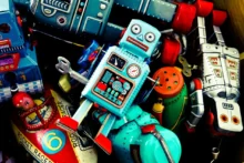 A collection of colorful vintage tin toys, including a central blue robot with bright details and a smiling face. Surrounding it are various toy cars, rockets, and other robots, creating a nostalgic and playful scene.