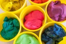 Top view of seven yellow cups each filled with colorful modeling clay in shades of yellow, red, purple, green, blue, light green, and pink, arranged closely together.