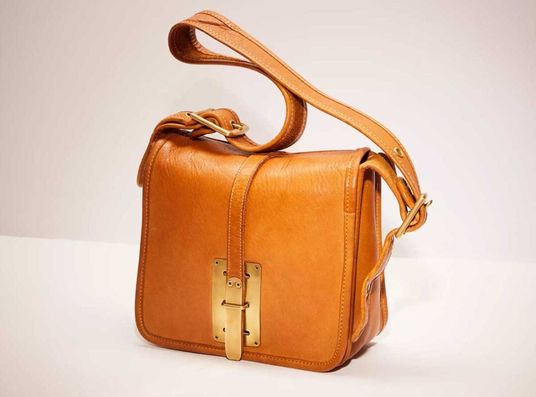 A tan leather shoulder bag with a gold buckle and clasp detail on the front, featuring an adjustable strap, displayed against a plain light background.