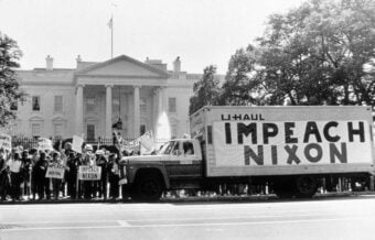 A large crowd protests in front of the White House, holding signs. A U-Haul truck with &ldquo;IMPEACH NIXON&rdquo; painted on its side is parked in front of the group. Trees and the White House appear in the background.