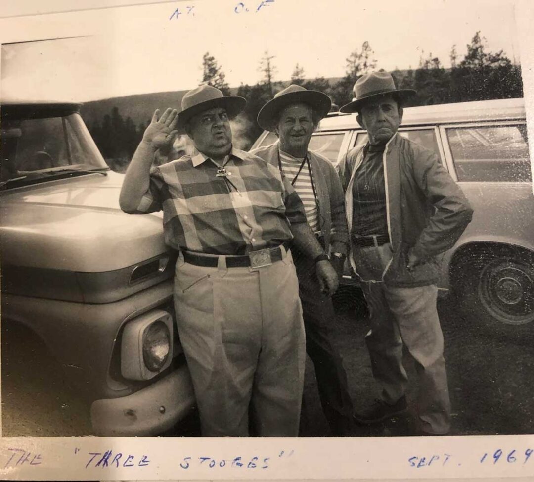 Three men dressed as the Three Stooges pose beside a vintage car in an outdoor setting, with trees in the background. The photo is labeled “The Three Stooges” and dated September 1964.