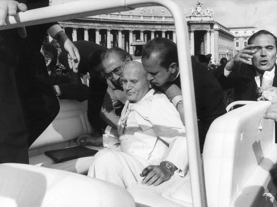 Pope John Paul II sits in a vehicle surrounded by concerned men after the 1981 assassination attempt in St. Peter’s Square, Vatican City. The Pope appears injured and is being supported by aides.