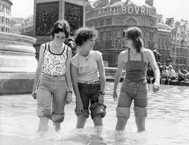 three young women in a fountain in london with their pants rolled up