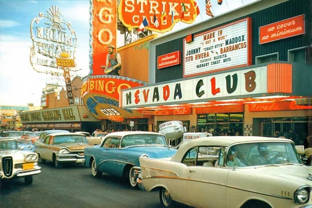 Colorful 1950s street scene in Las Vegas, with vintage cars driving past neon signs and casino marquees, including the Nevada Club and Binion’s Gambling Hall, under a bright, bustling atmosphere.