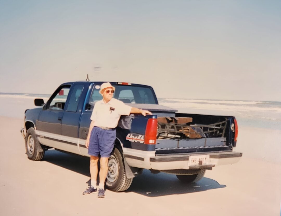 man standing with a blue 1990s pickup truck