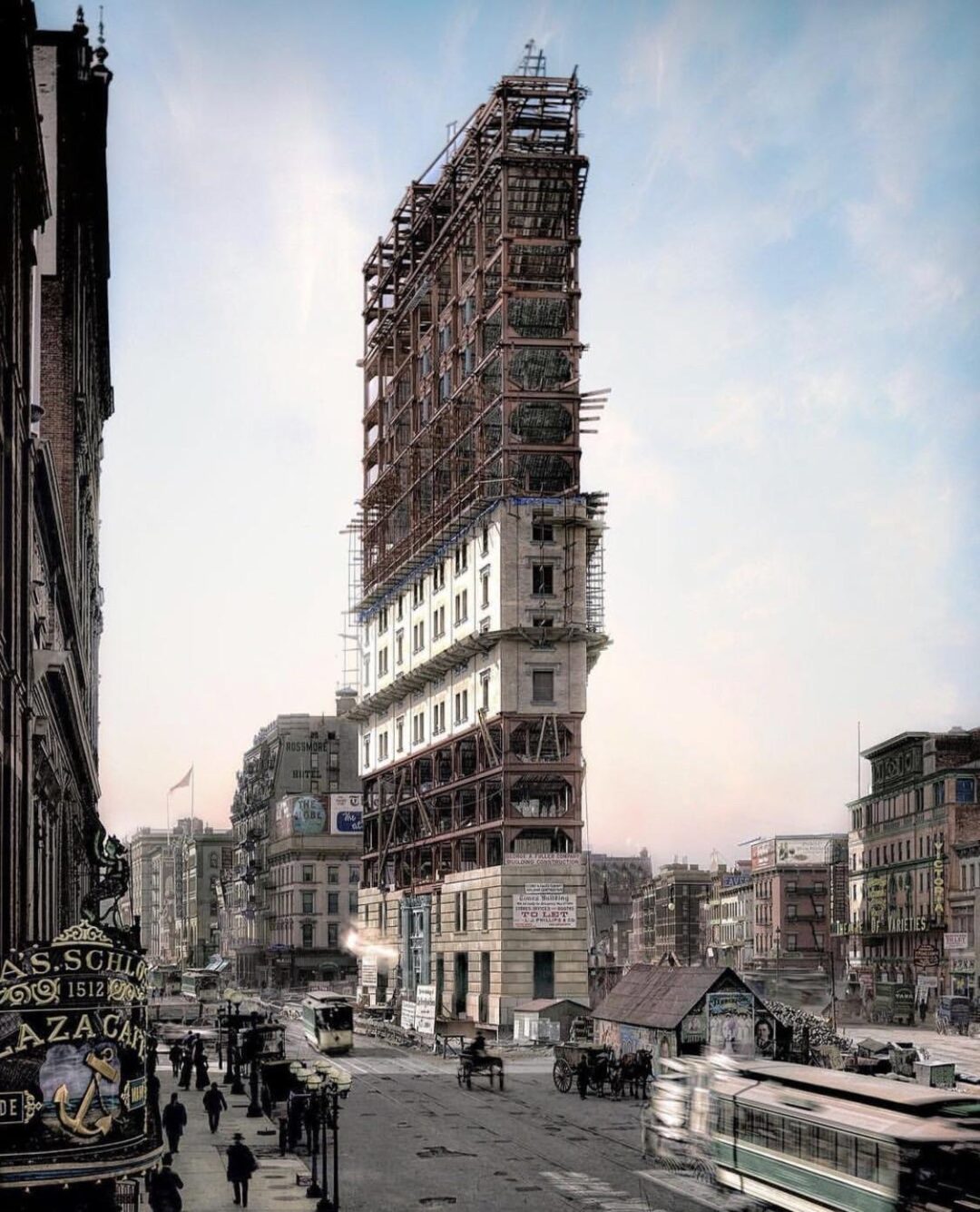 A tall building under construction towers over a busy city street with scaffolding covering its upper floors. Pedestrians, horse-drawn carriages, and early automobiles fill the lively urban scene.