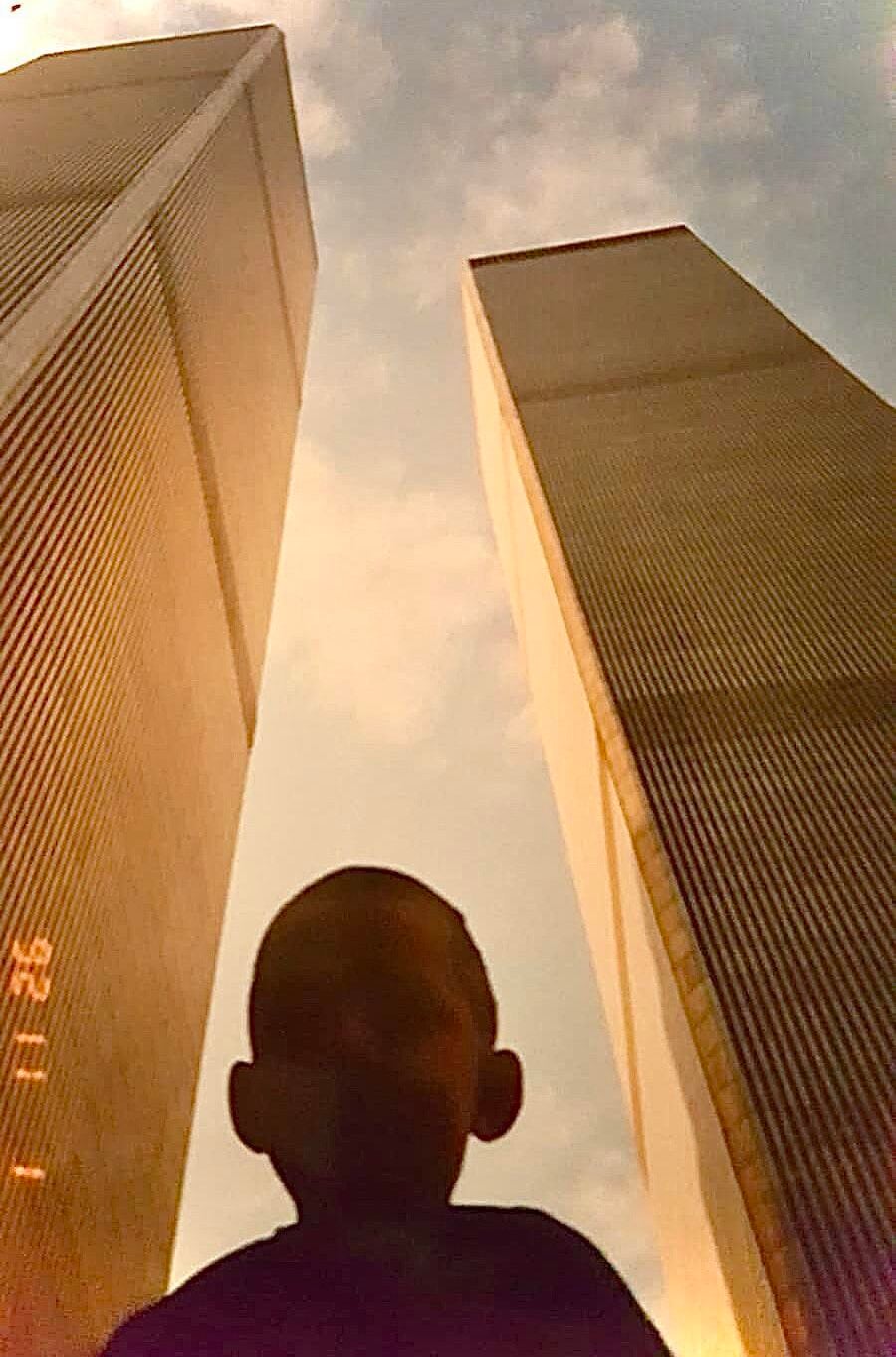 A silhouette of a child stands in the foreground with the Twin Towers of the World Trade Center rising on either side against a partly cloudy sky.