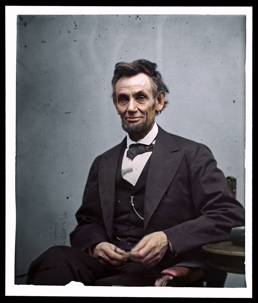 A historic portrait of Abraham Lincoln seated, wearing a dark suit and bow tie, looking slightly to the side with a neutral expression against a plain background.
