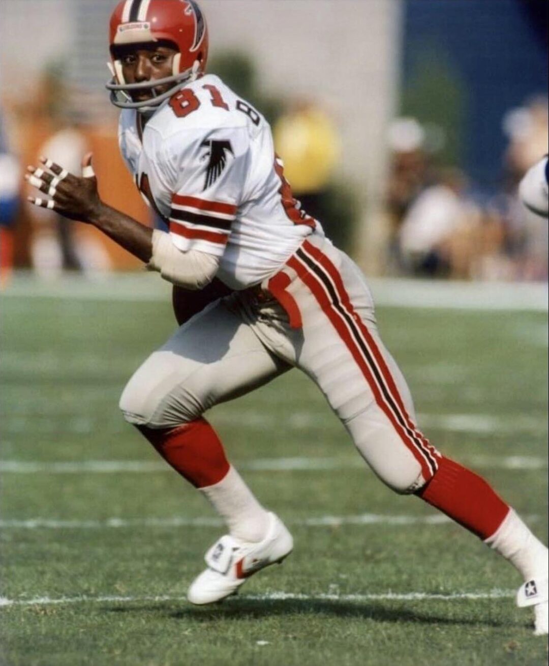 A football player in a red and white Atlanta Falcons uniform, number 81, runs with the ball on a grassy field during a game. He appears focused and is looking upfield.