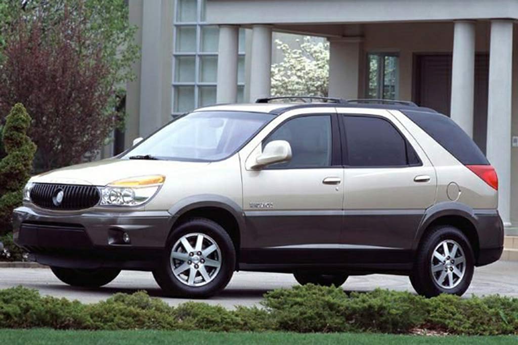 A beige and gray SUV parked in front of a modern house with large windows and greenery around.