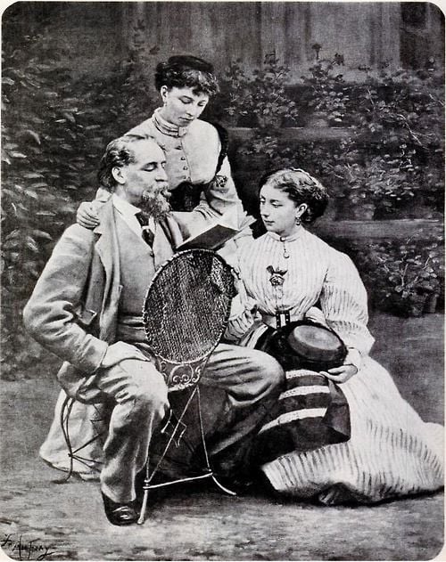 A vintage black-and-white photo of three people; a seated man holding a tennis racket, a seated woman beside him holding a hat and racquet, and a standing woman behind them, all wearing Victorian-era clothing.