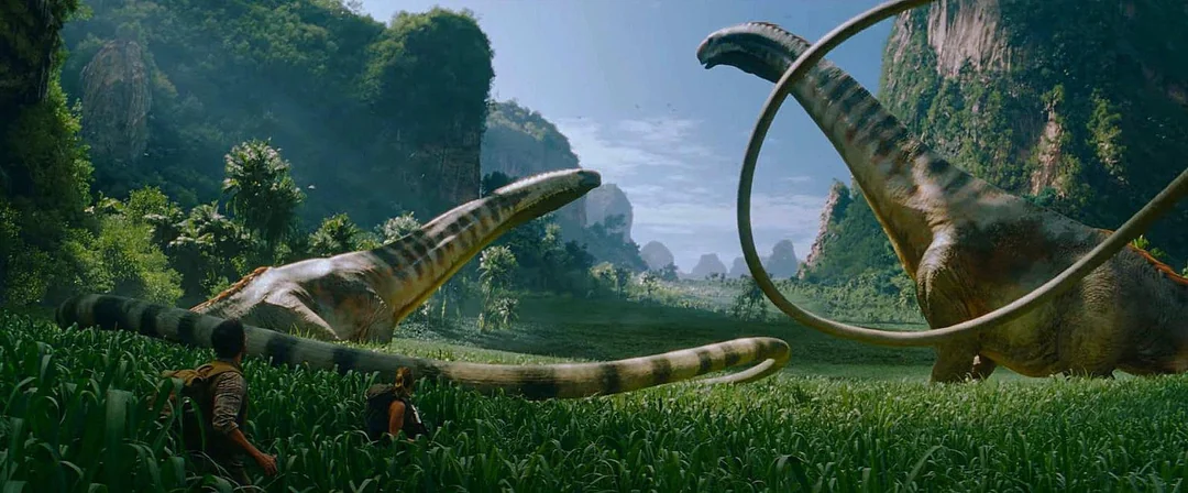 Two people stand in tall grass facing three enormous long-necked dinosaurs in a lush, green valley surrounded by cliffs and dense jungle under a bright blue sky.