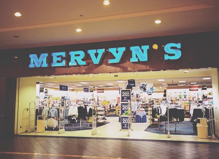 Storefront of Mervyn’s in a shopping mall, with illuminated blue letters above the entrance and clothing displays visible inside the brightly lit store.