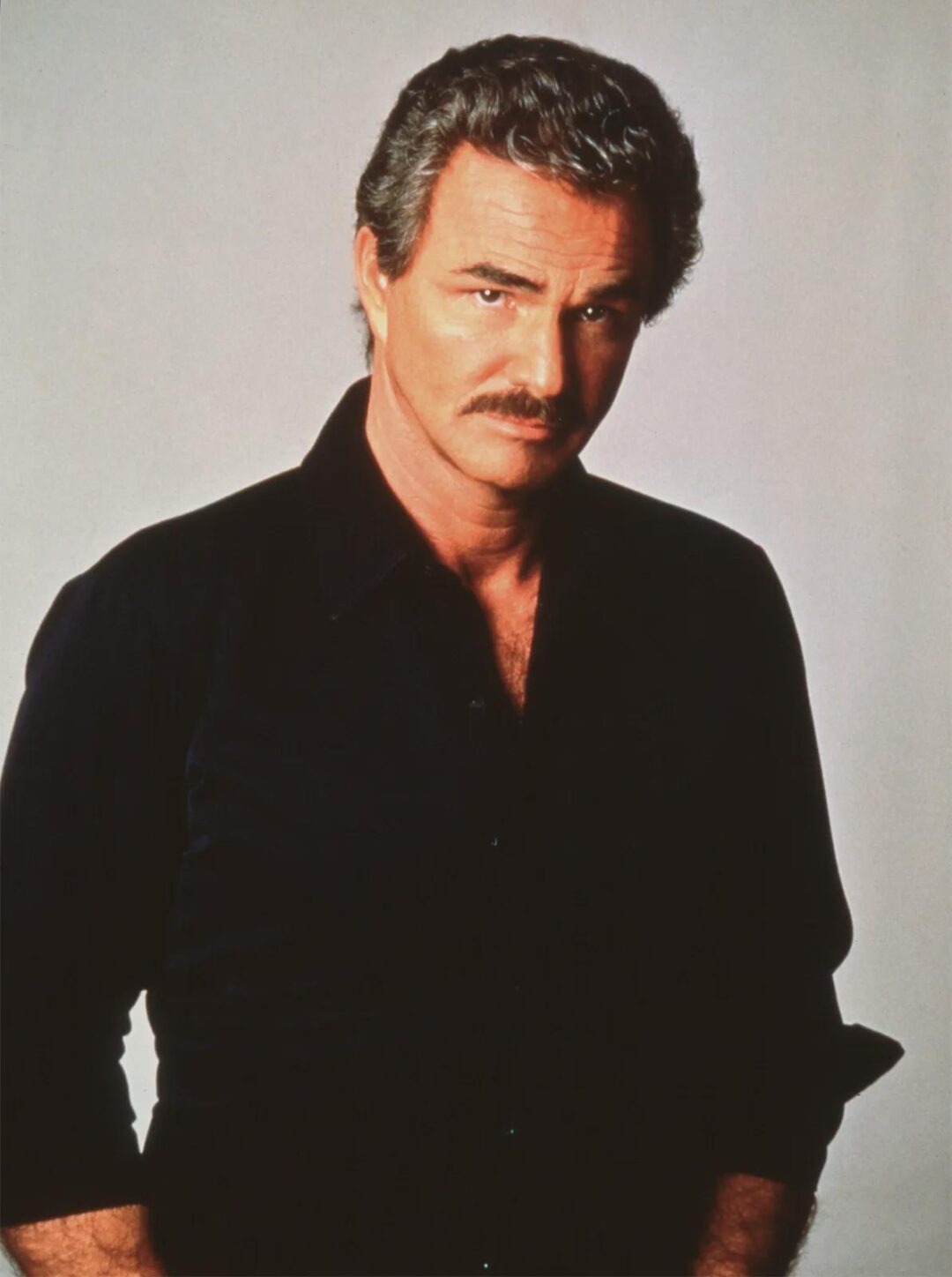 A middle-aged man with short, wavy dark hair and a mustache poses against a plain background. He wears a black collared shirt and looks confidently at the camera with a neutral expression.