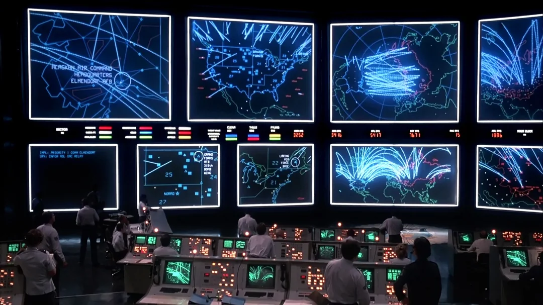 A control room with people at computer consoles monitors multiple large screens displaying maps, flight paths, and data, including missile trajectories over North America and Eurasia. The scene is tense and technological.