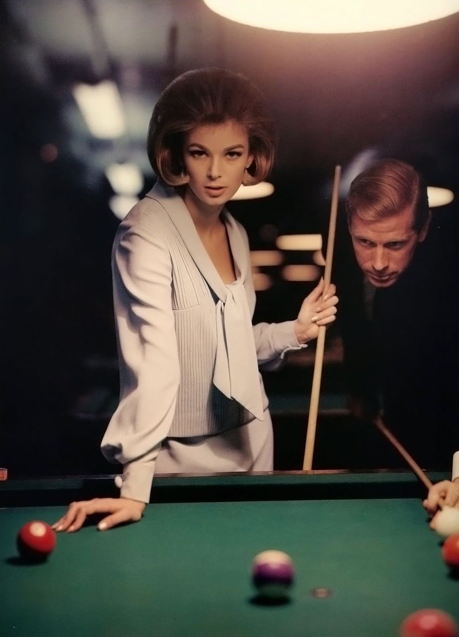 A stylish woman in a light suit leans over a pool table, holding a cue, while a man in a dark suit stands behind her, watching intently. The scene is dimly lit with a focused overhead light.