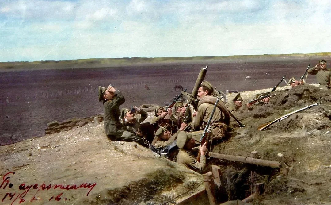 A group of soldiers in World War I-era uniforms take cover in a trench, aiming rifles and peering over the edge, with a vast, barren landscape and cloudy sky in the background.