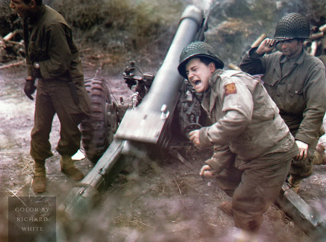 Three WWII soldiers operate an artillery gun in a muddy field. One covers his ears and flinches from the blast, another stands nearby, and the third adjusts his helmet, all wearing military uniforms and helmets.