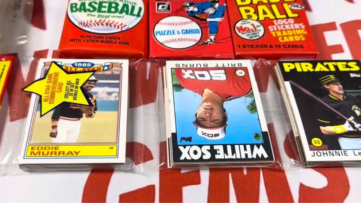 Several packs and stacks of vintage baseball cards are displayed on a table, including an Eddie Murray card, a White Sox card, and a Pirates card, all in protective sleeves.