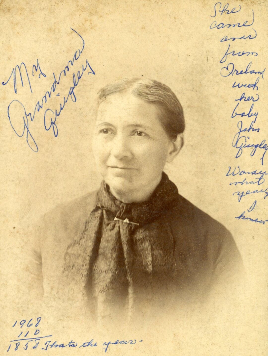 Sepia-toned portrait of an older woman wearing a dark dress and scarf. Handwritten notes surround the photo, including “My Grandma Quigley” and information about her coming from Ireland in 1855.