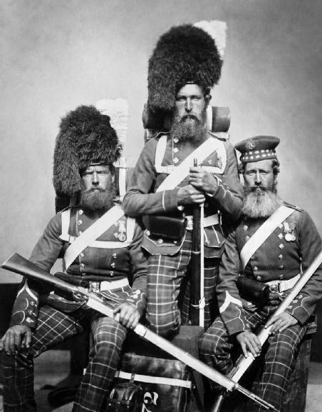 Three bearded soldiers in 19th-century Scottish military uniforms with tartan patterns and fur hats pose for a black-and-white portrait, holding rifles and wearing medals.