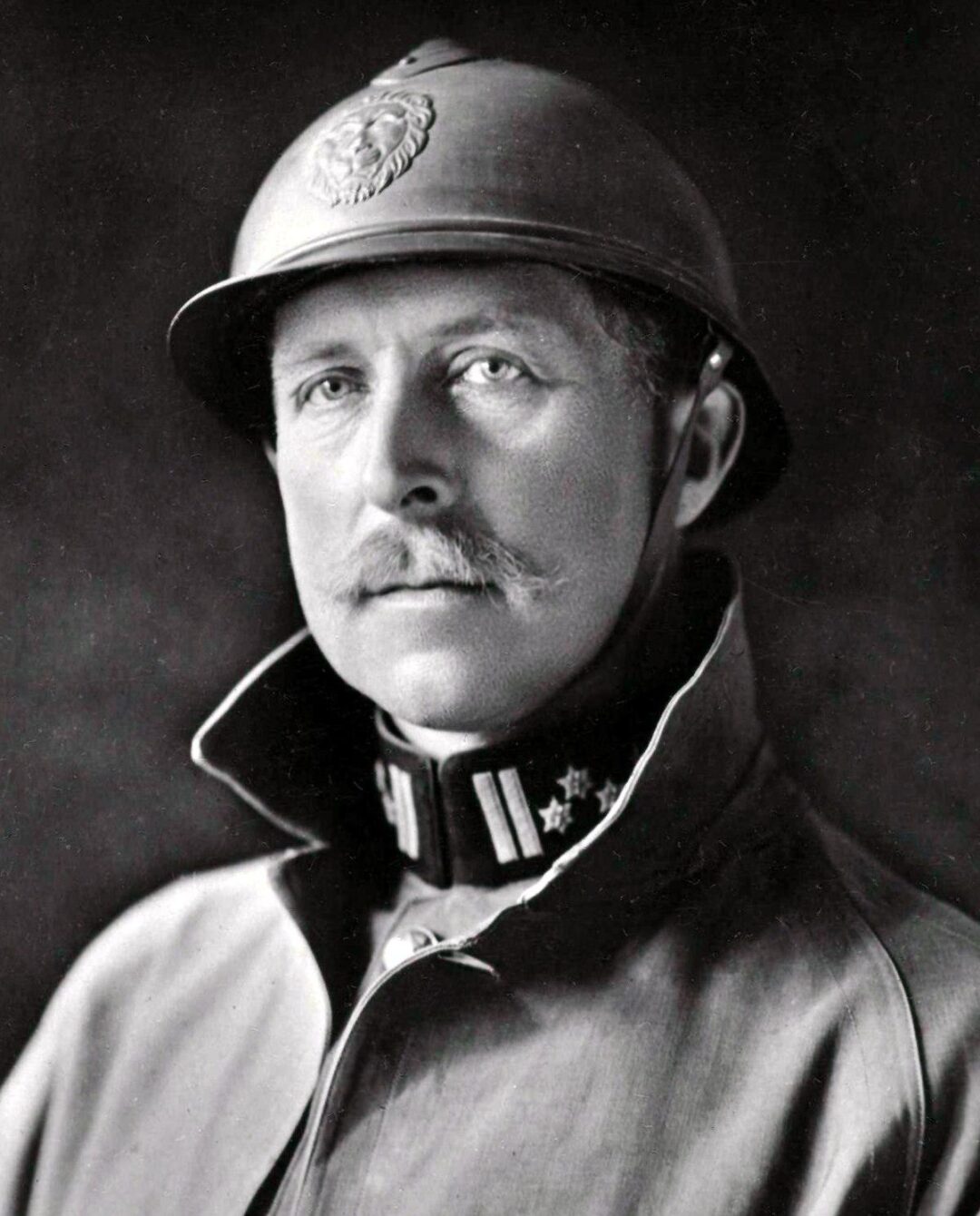 Black and white portrait of a man wearing a military uniform, including a high-collared coat and a helmet with an emblem. The man has a mustache and looks directly at the camera with a serious expression.