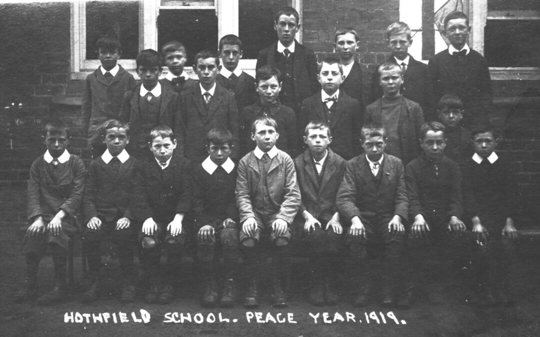 A black-and-white photo of a group of schoolboys and two adults posing in three rows in front of a brick building. Text at the bottom reads “Hothfield School. Peace Year. 1919.”