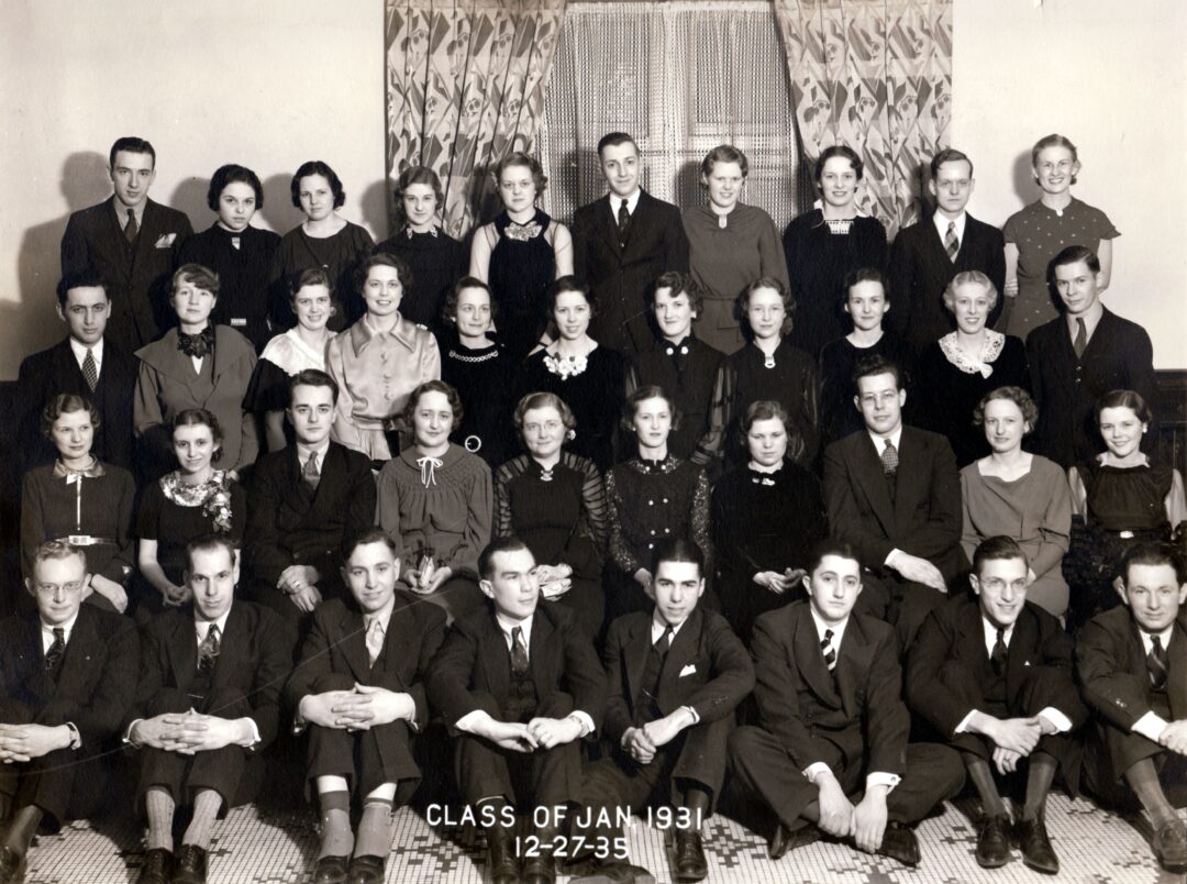 Black and white photo of a large group of young men and women in formal attire, posed in rows for a class portrait labeled "Class of Jan 1931" with the date "12-27-35" at the bottom.