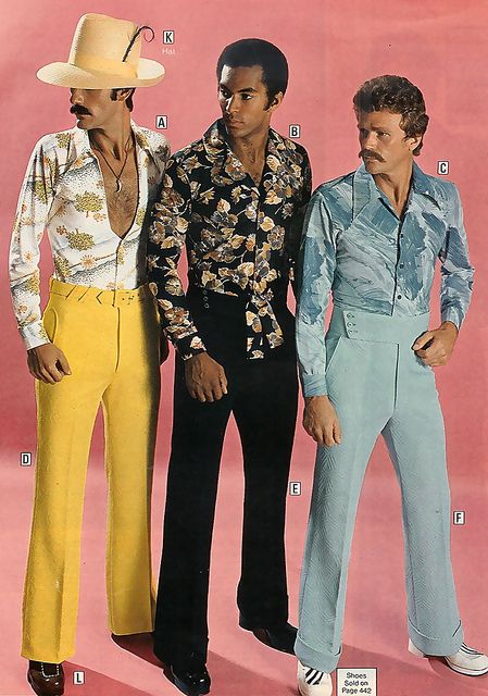 Three men stand against a pink background wearing 1970s fashion: one in a large hat, floral shirt, and yellow pants; one in a dark floral shirt and black pants; and one in a blue patterned shirt and light blue pants.