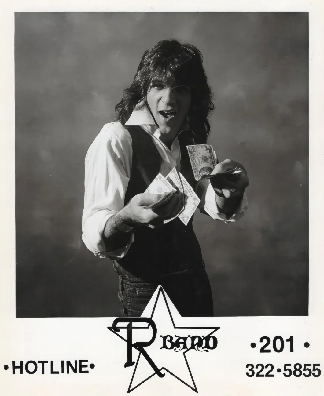 A man with long hair, wearing a vest and white shirt, excitedly holds and fans out several dollar bills. The text below reads “HOTLINE • 201-322-5855” with a stylized star logo and the word “Ragno.”