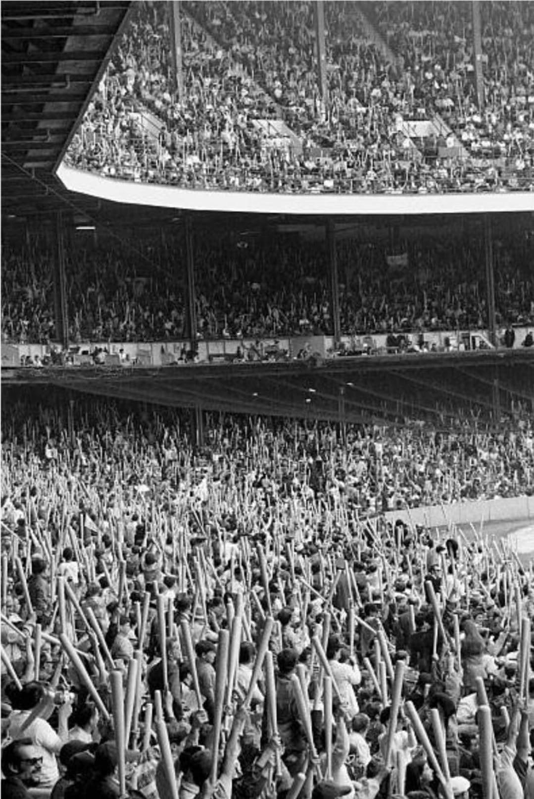 A black-and-white photo of a baseball stadium packed with fans, many of whom are holding up inflatable baseball bats, creating a dense sea of sticks throughout the crowded stands.
