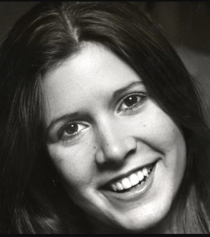 A young woman with long, straight hair smiles at the camera. The black-and-white photo is a close-up, showing her clear, expressive eyes and teeth.