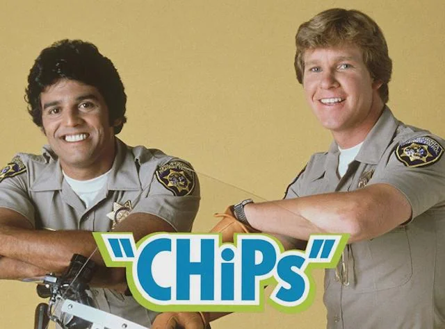 Two smiling male police officers in uniform pose in front of a yellow background with the "CHiPs" TV show logo in front of them.