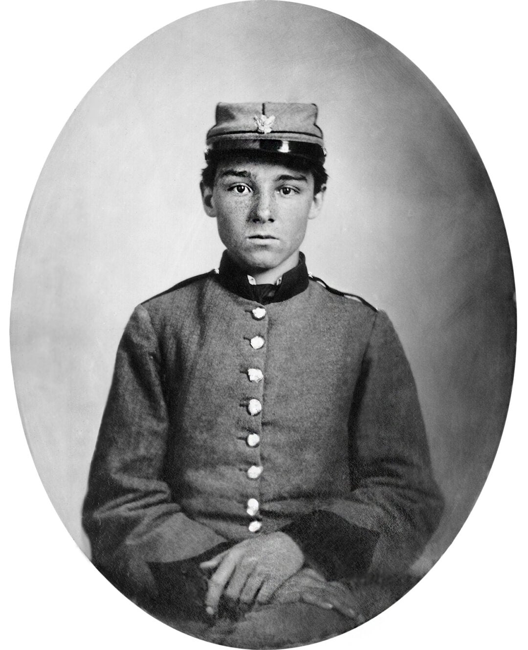 Black-and-white portrait of a young soldier in a military uniform and cap, seated and facing forward, with a neutral expression. The image is framed in an oval shape.
